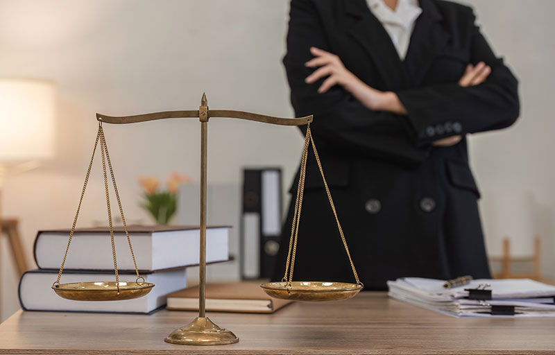 Attorney standing with arms folded with scales of justice in foreground.